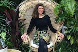 Lawyer-turned-indoor landscaper Alice Crowe sits on a rattan chair among a variety of lush plants.