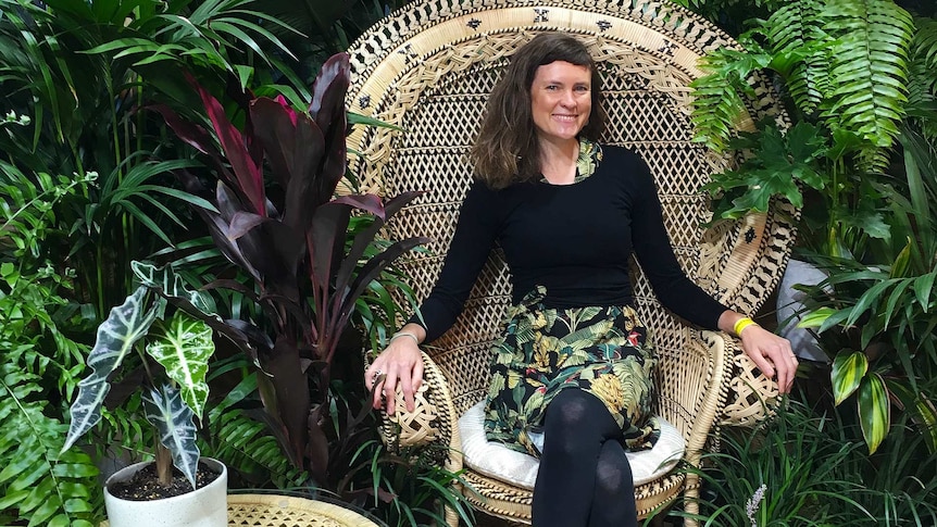 Lawyer-turned-indoor landscaper Alice Crowe sits on a rattan chair among a variety of lush plants.