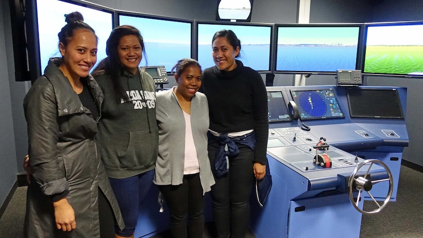 Four female AMC students in front of a ship simulator