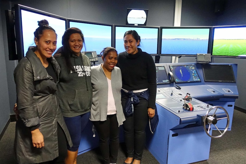 Four female AMC students in front of a ship simulator