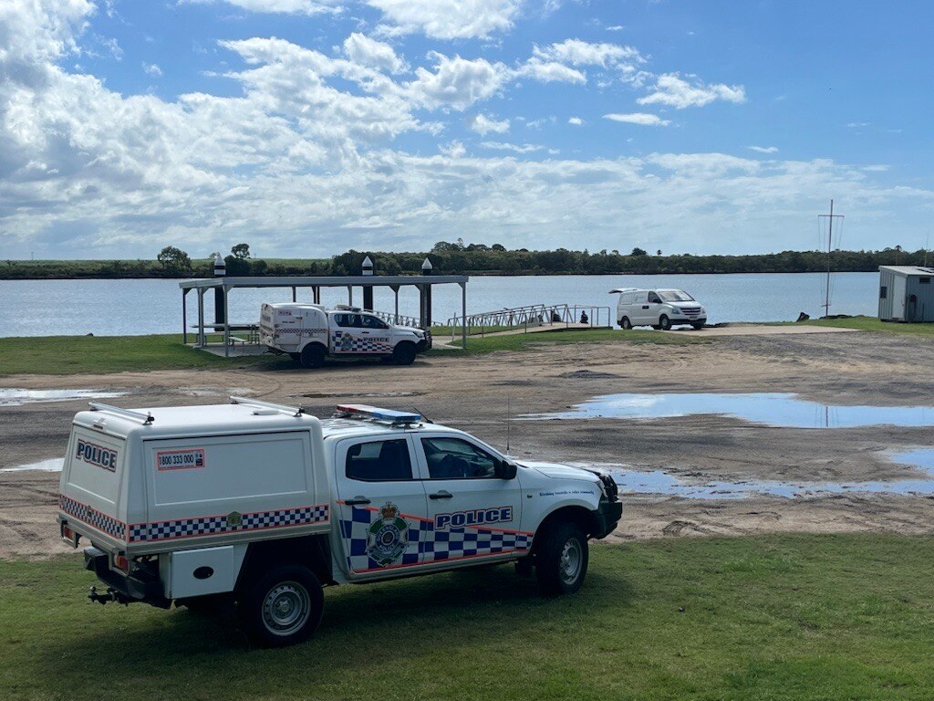 Three police cars by the side of the river, parked on gravel and grass in front of a jetty and a boat ramp.