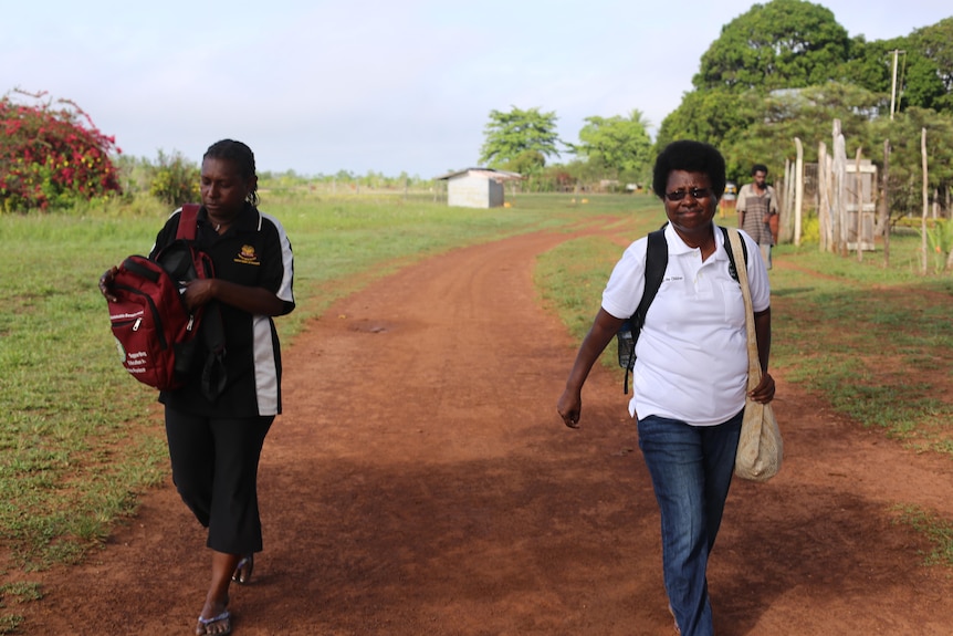 Bernadette and a colleague walk down a dirt road in a rural area