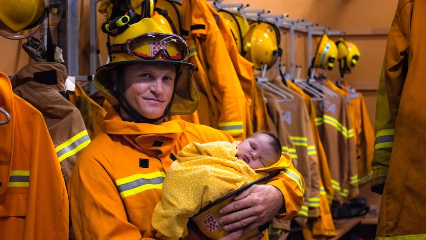 Man in yellow firefighting suit holding newborn baby