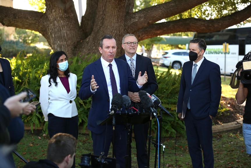 A wide shot showing Mark McGowan talking at a media conference outdoors with Anthony Albanese and others surrounding him.