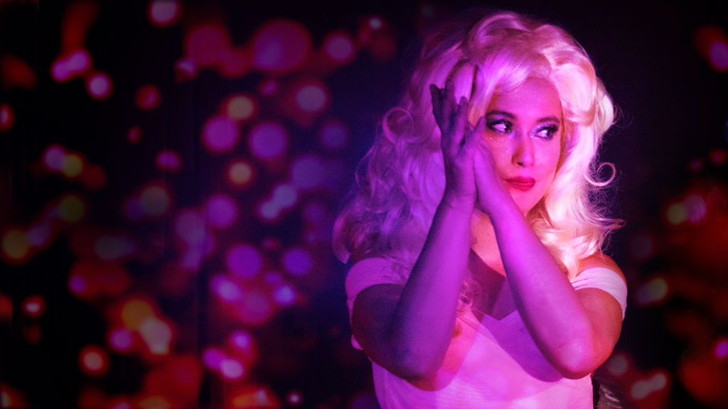 Elly-May Barnes with her hands up near her face, wearing blonde cabaret wig.