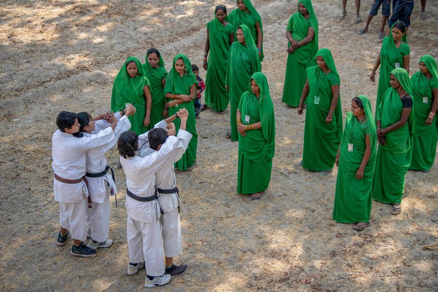 A group of women in green saris watch men in karate uniforms