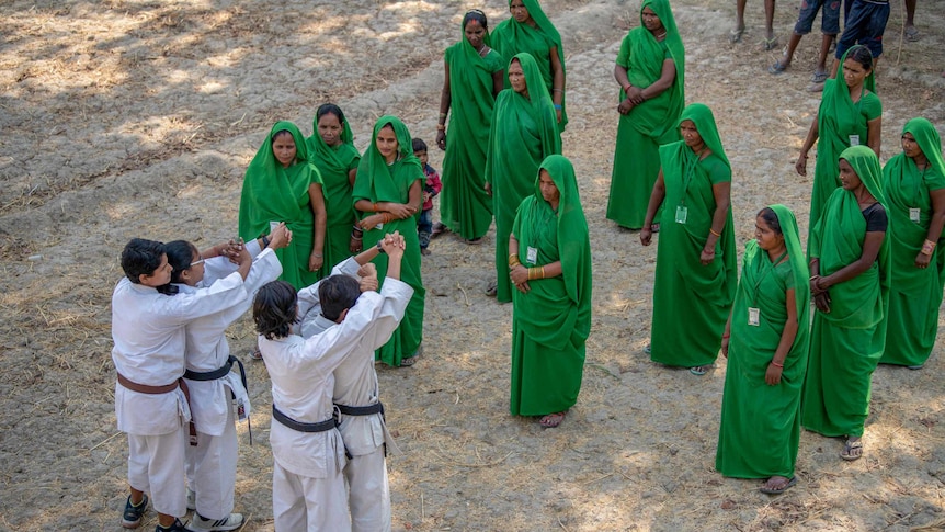 A group of women in green saris watch men in karate uniforms