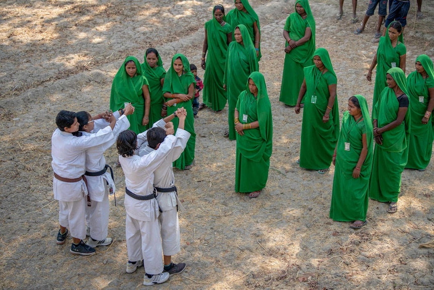 A group of women in green saris watch men in karate uniforms