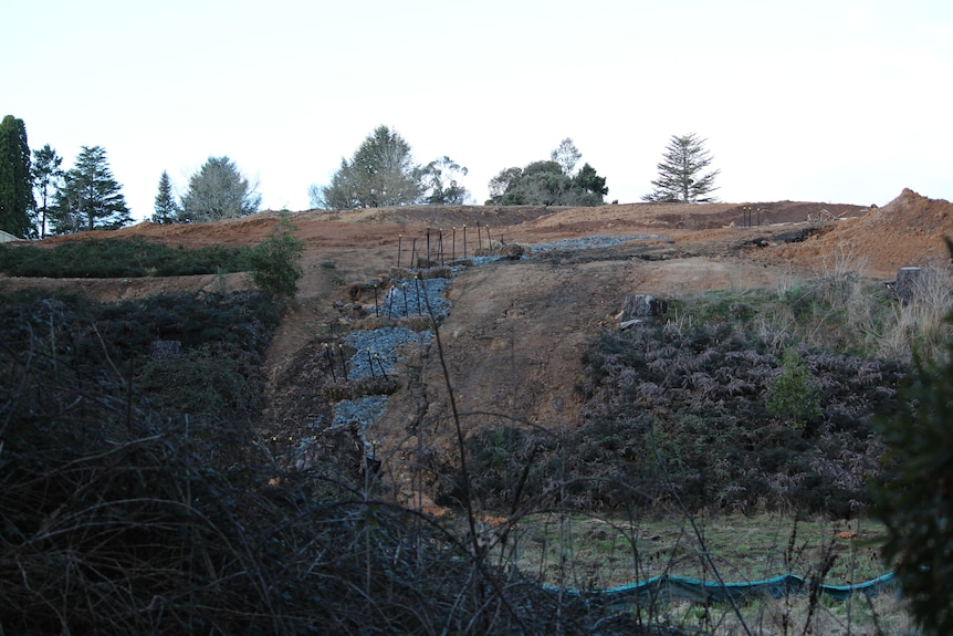 A hill that has been cleared of vegetation and left with orange clay-like topsoil. 
