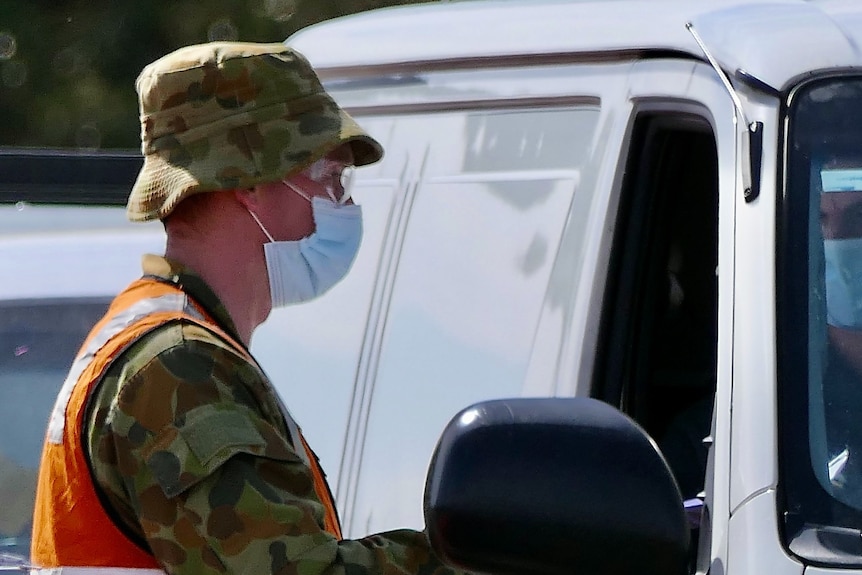 An ADF officer, wearing a mask speaks to a van driver through the window.