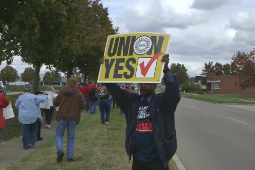A man stands with a sign saying "Union: yes" at a protest