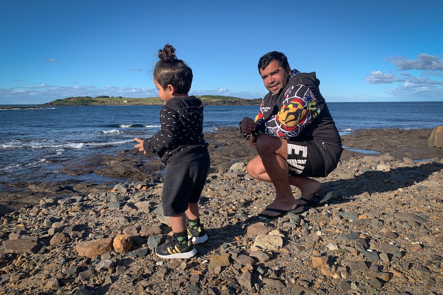   a man and a young child outdoors standing on rock by the sea