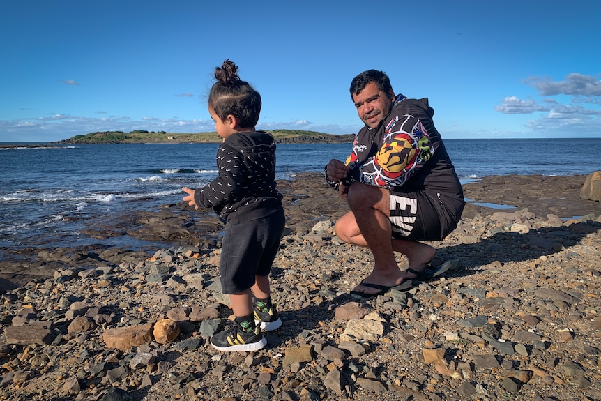  a man and a young child outdoors standing on rock by the sea