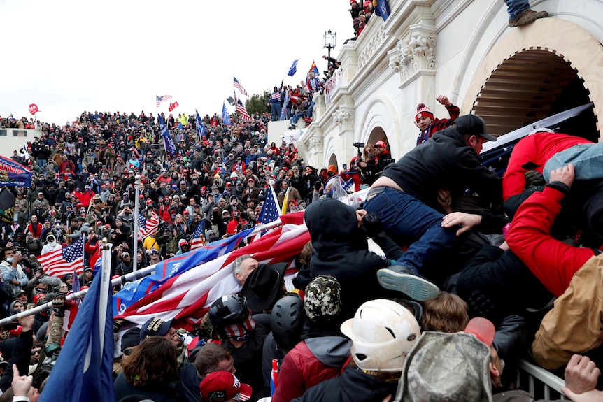 A mass of Donald Trump supporters swarm up the steps of the US Capitol as some attempt to gain entry through a blocked archway.