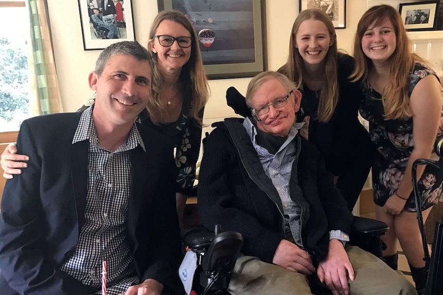 A man and three woman stand behind another man in a wheelchair