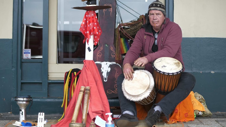 A man busks with djembes on a street