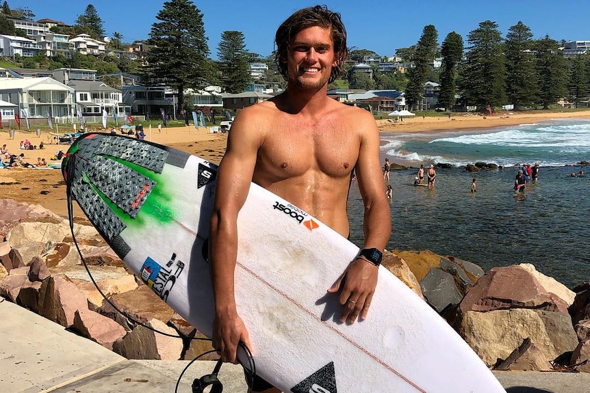 Cooper Cronk smiling while holding a surfboard looking at the camera.