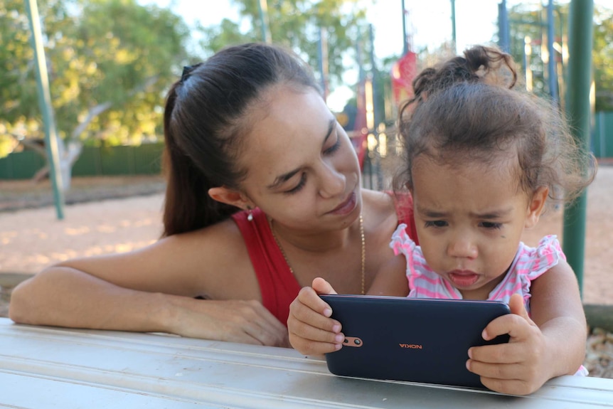 Caitlyn Roe at a playground with her daughter, looking at a phone.