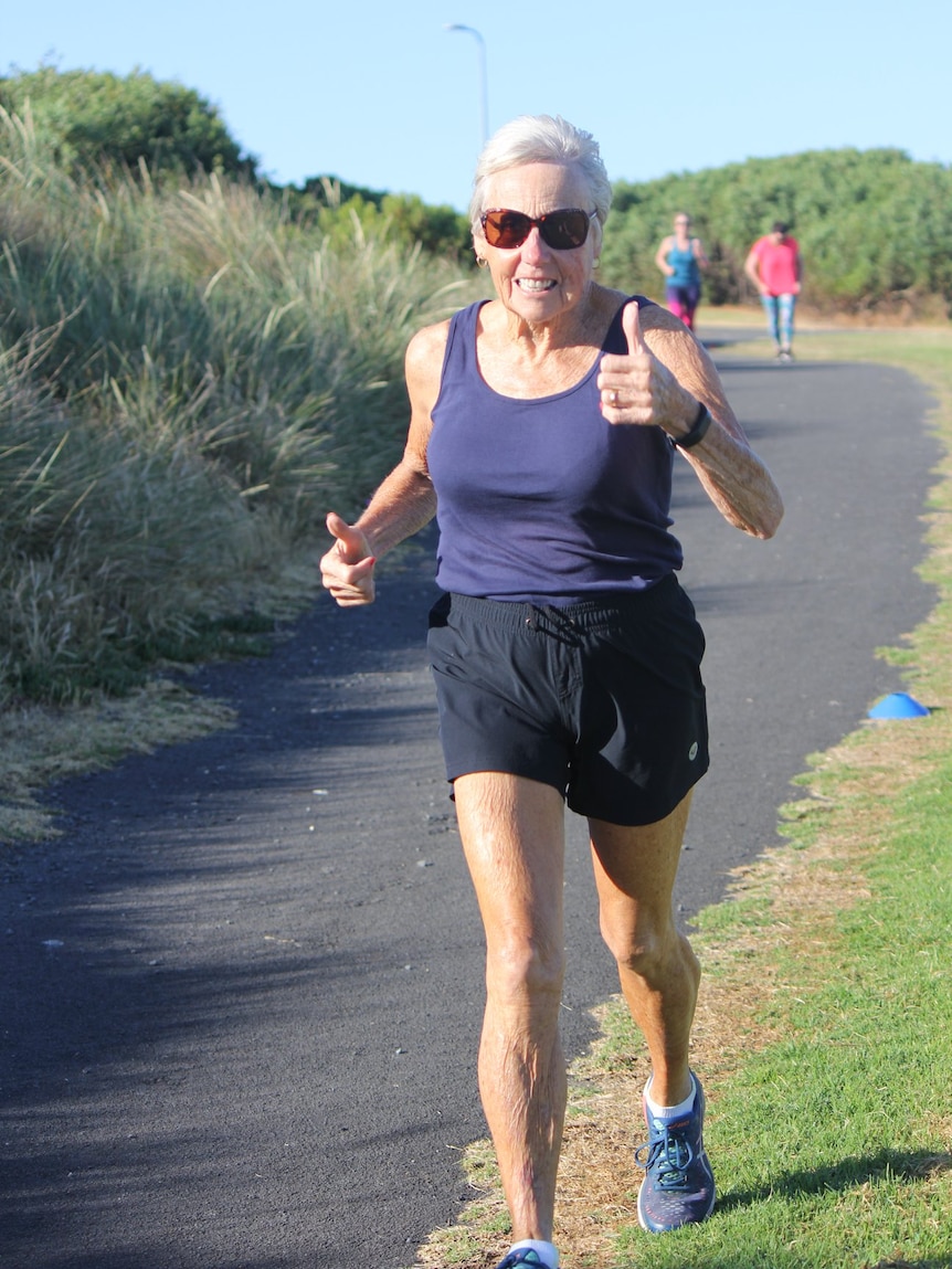 Judy Amoore Pollock gives a thumbs up as she runs in shorts and a singlet.