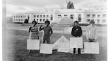 A black and white photo of four men standing in front of Old Parliament House, holding signs