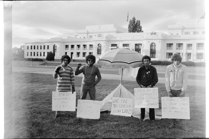 A black and white photo of four men standing in front of Old Parliament House, holding signs