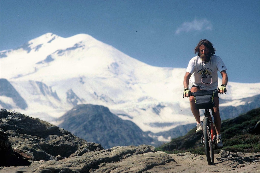 Cyclist with long hair and bushy beard with snowy mountain in the background