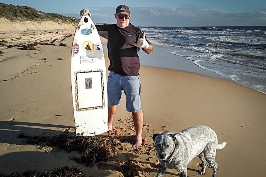 Man holding mini boat on a beach in Western Australia with a dog