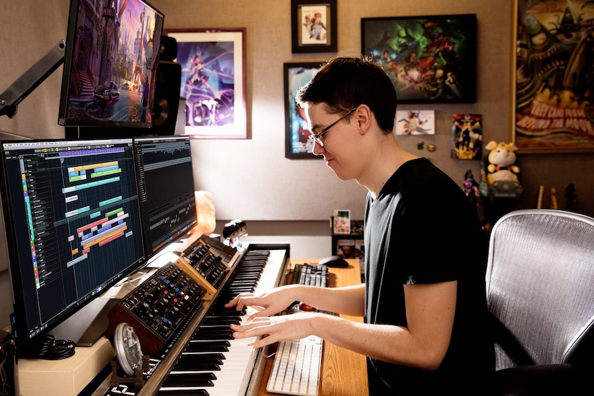 A musicians sits at a keyboard and computer screens surround by computer games images.