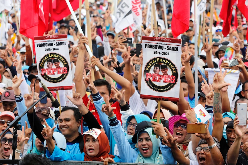 Men and women in hijabs wave flags, chant and gesture during a political rally.