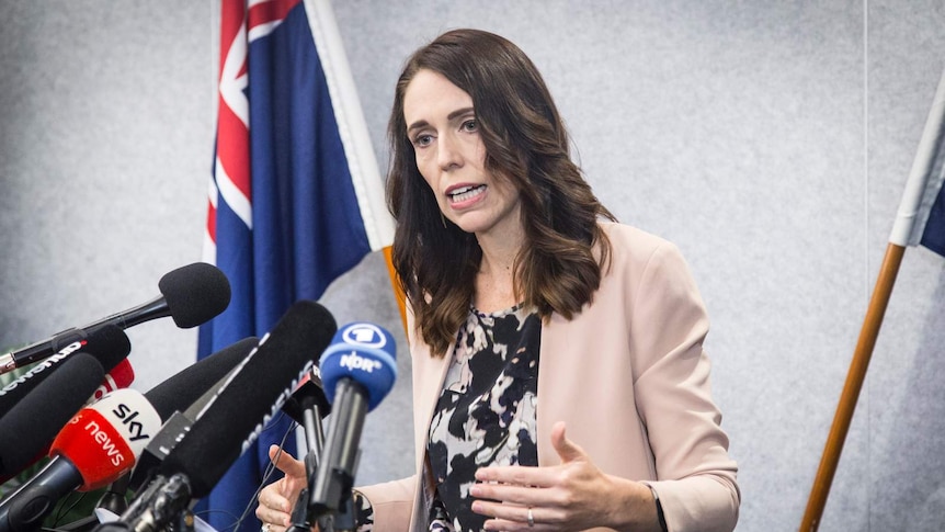 Jacinda Ardern speaks as she stands at a lectern in Christchurch next to the New Zealand flag.