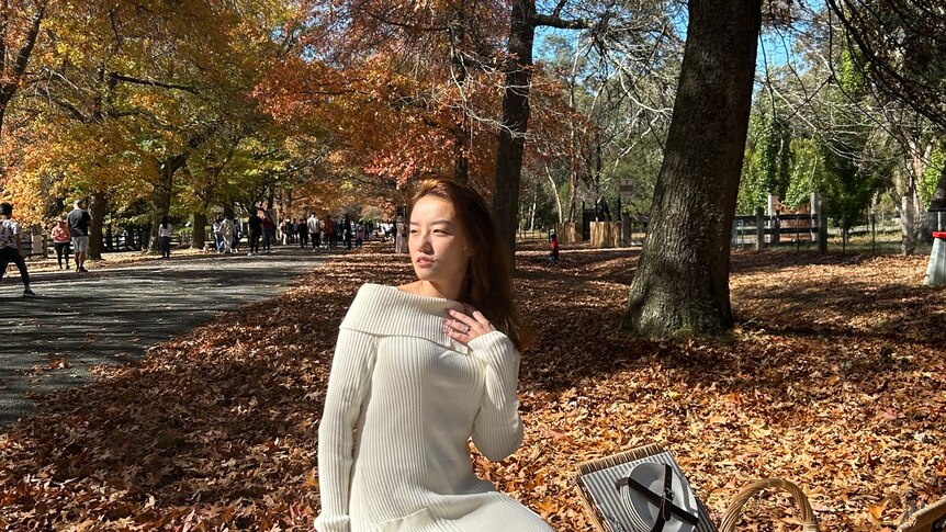 A woman sits on a picnic rug under autumn trees. 