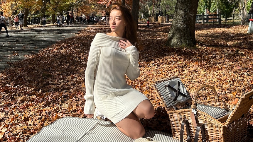A woman sits on a picnic rug under autumn trees. 