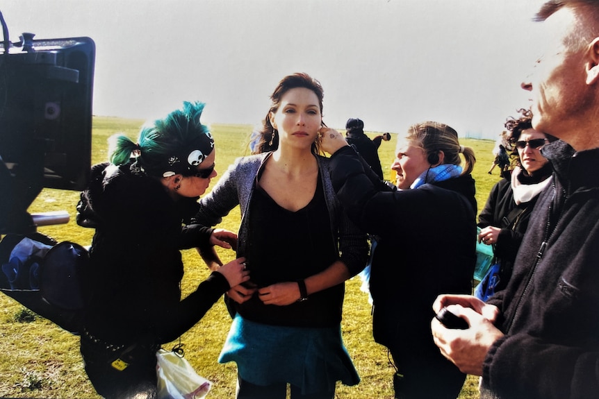 Claudia Karvan stands in a field as crew members surround her to check her audio, make-up and accessories.