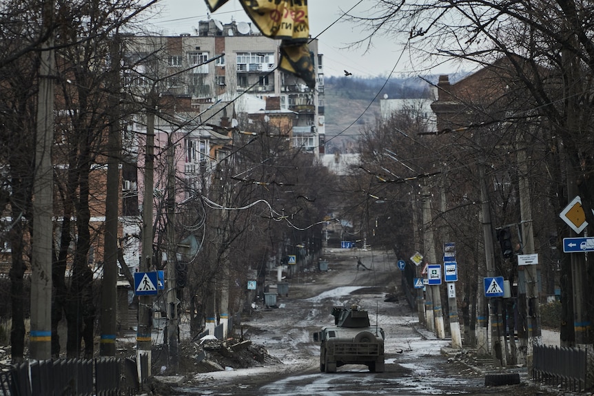 Ukrainian soldiers ride in a Humvee in Bakhmut through a damaged street.