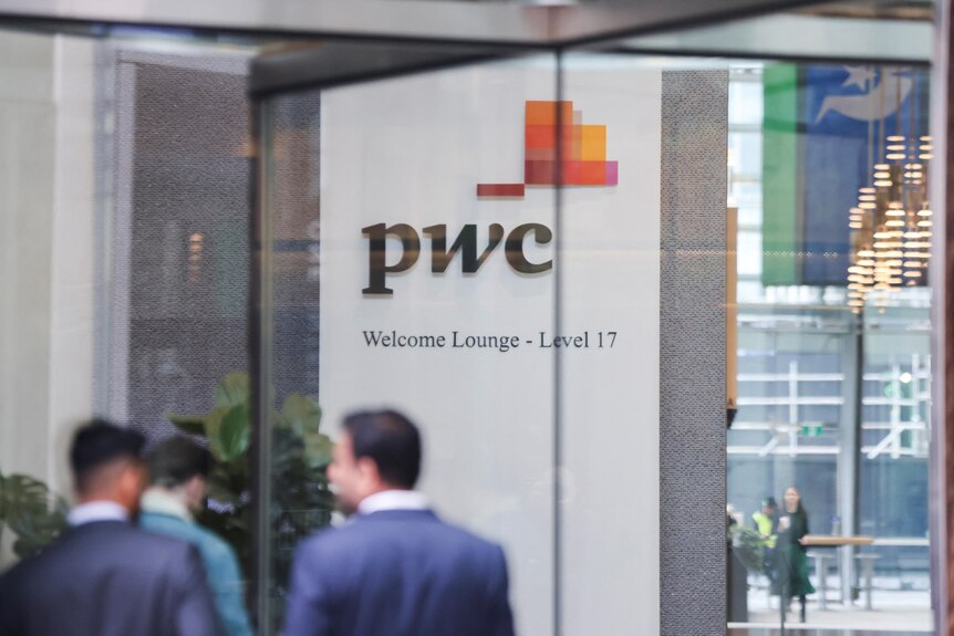 A PwC logo on a wall seen through a spinning glass door with obscured people in suits in the foreground.