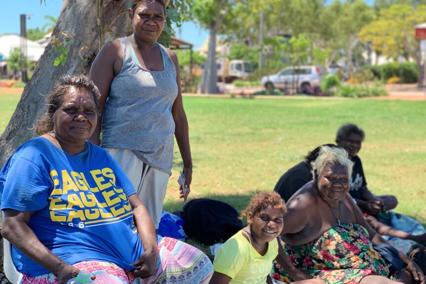 A group of Aboriginal women sit together on the grass under the shade of a tree in Broome.