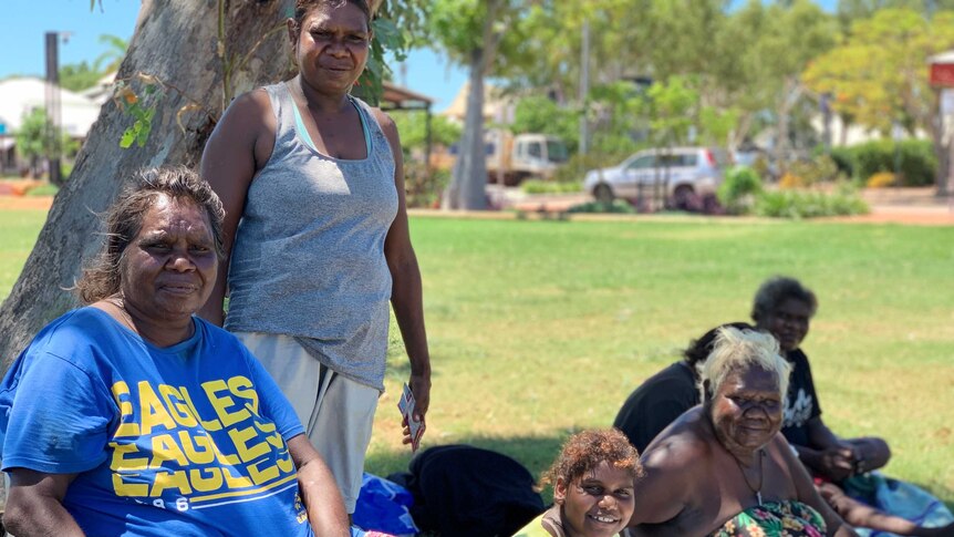 A group of Aboriginal women sit together on the grass under the shade of a tree in Broome.