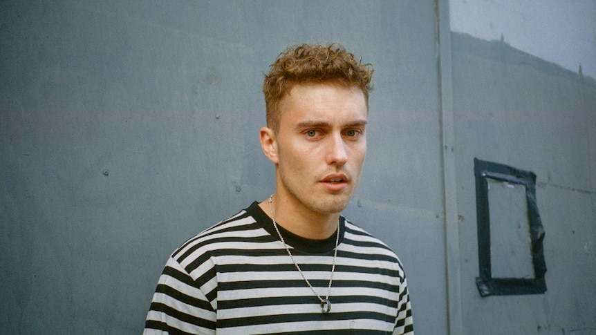 Sam Fender, dressed in black and white striped tee shirt, wearing silver chain with ring attached