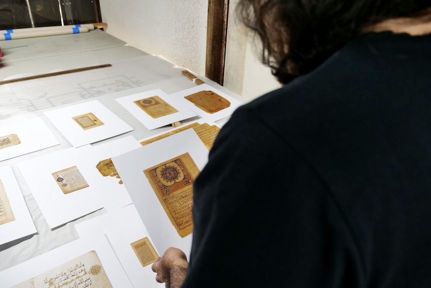 A man holds print-outs of ancient Quran pages