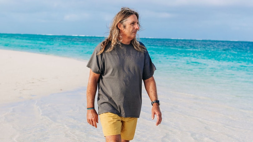 Man walks along white sand of beach with turquoise blue water