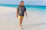 Man walks along white sand of beach with turquoise blue water