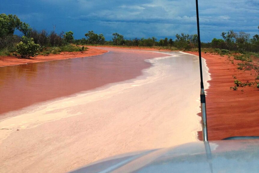A stream of knee-deep water covers a remote red dirt road