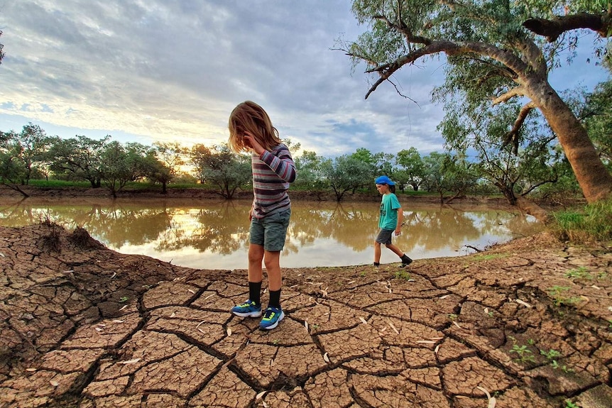 Two children stand beside a cracked earth and a dam at sunset Lass O'Gowrie homestead near Charleville in Queensland.