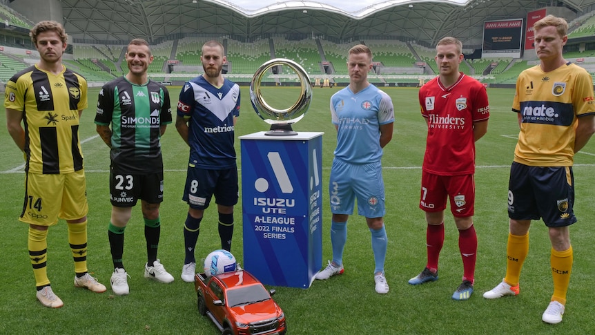 Six A-League Men's players stand next to the Championship trophy.
