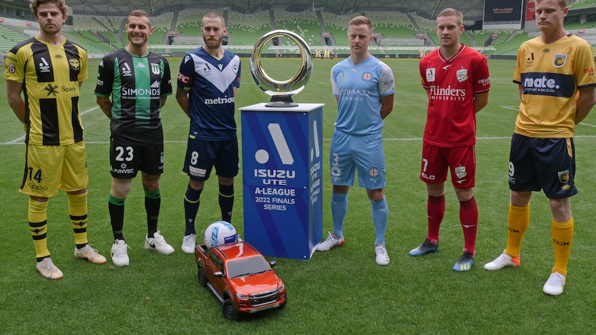 Six A-League Men's players stand next to the Championship trophy.