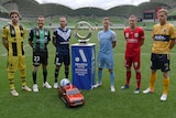 Six A-League Men's players stand next to the Championship trophy.