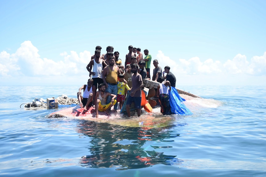 Rohingya refugees stand on their capsized boat before being rescued in the waters off West Aceh, Indonesia. 