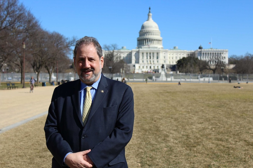 A man in a suit stands on the lawn in front of the US capitol building