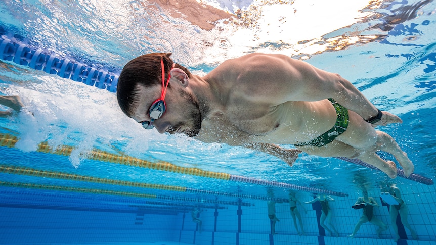 Blake swimming underwater holding his breath gliding with other athletes holding onto the edge of the pool behind