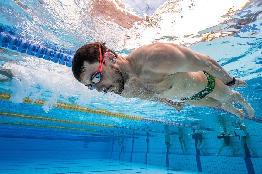 Blake swimming underwater holding his breath gliding with other athletes holding onto the edge of the pool behind